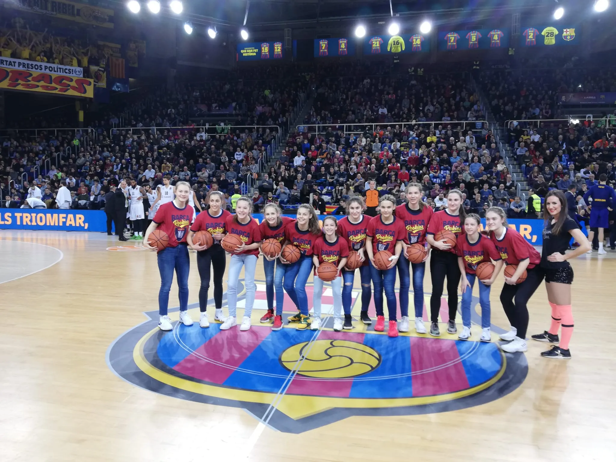 A girls' team lined up on the Palau Blaugrana court in front of a full crowd