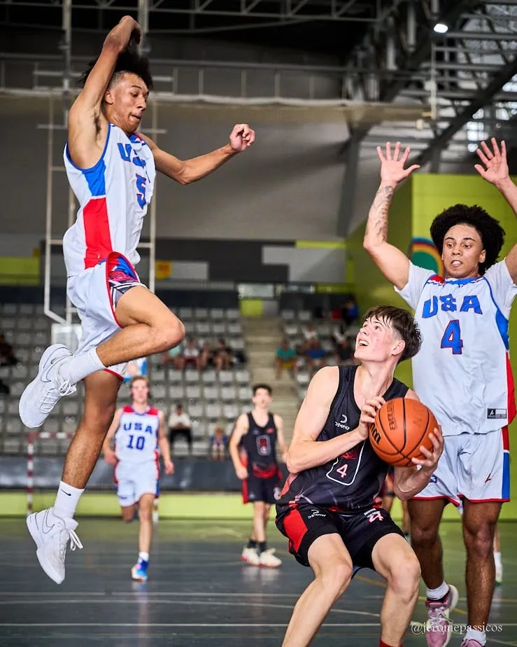 A player driving with the ball as a defender leaps across to block