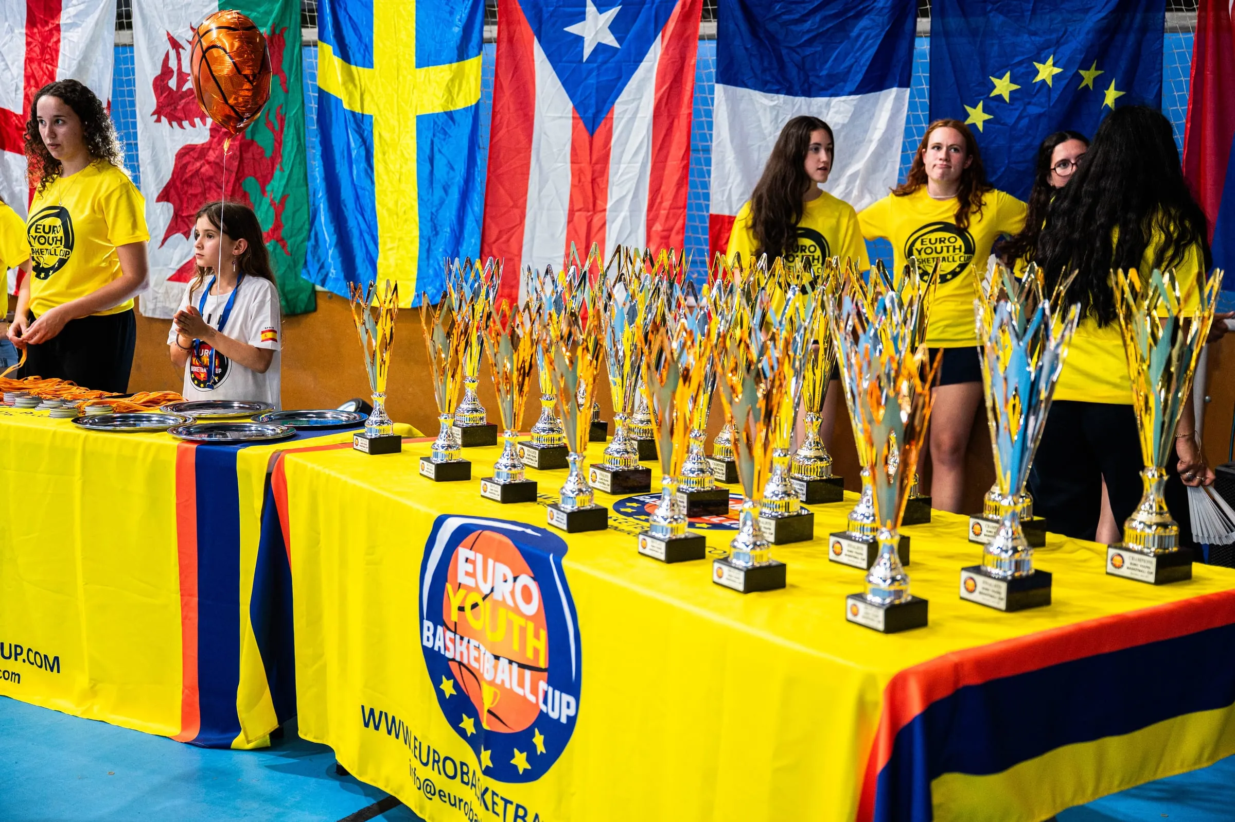 Volunteers behind the trophy table under the flags of the competing nations